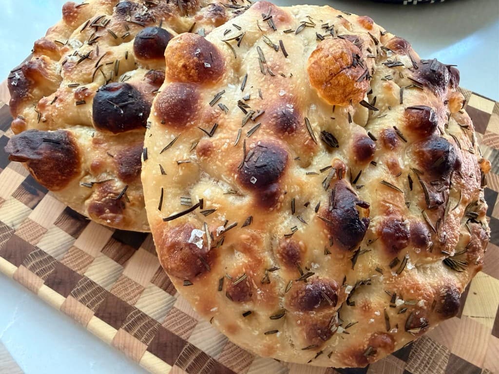 Rosemary focaccia loaves with coarse salt on a wooden board